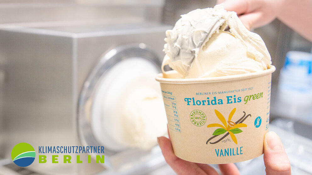 Ein Mensch füllt eine Kugel Eis in einen Pappbecher. 