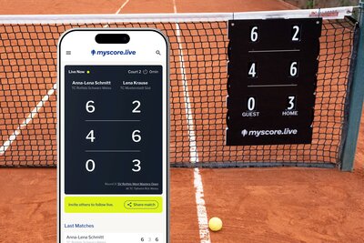 Auf dem Bild sieht man im Hintergrund einen Tennisplatz. Im Vordergrund ist ein Handy zu sehen, dass den Spielstand anzeigt.