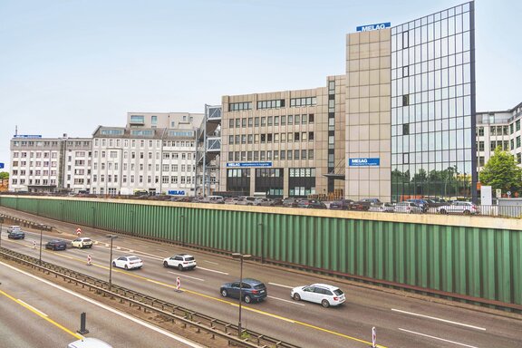 Zu sehen ist eine Stadtautobahn vor einer Wärmschutzwand, dahinter ein Wohngebiet.