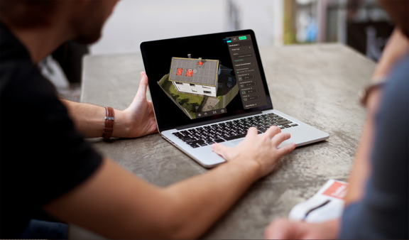 Zwei Personen betrachten auf einem Laptop eine 3D-Darstellung eines Hauses mit markierten Bereichen auf dem Dach.