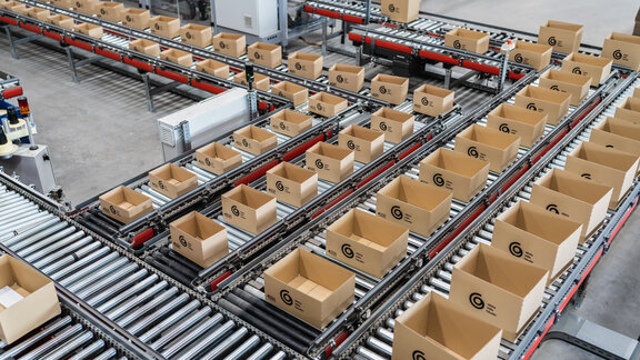Viele kleine Kartons stehen auf Rollfließbändern