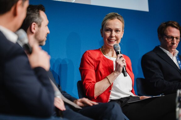 Manja Schreiner spricht in einem Mikrofon zu anderen Personen auf der Bühne.