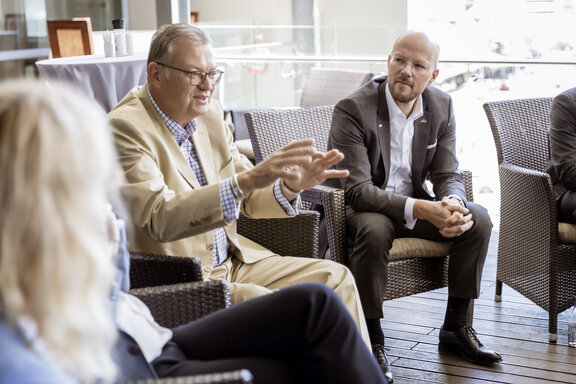 Mehrere Personen sitzen in einer Gesprächsrunde. Eine Person spricht und gestikuliert, während andere zuhören.