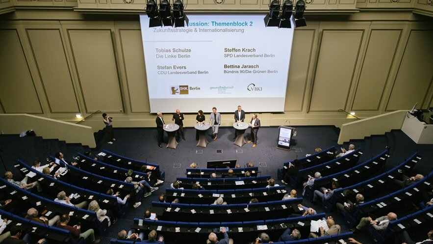 Ein Auditorium mit Gästen des wahlpolitischen Dialogs und die Diskutanten vor einer Leinwand