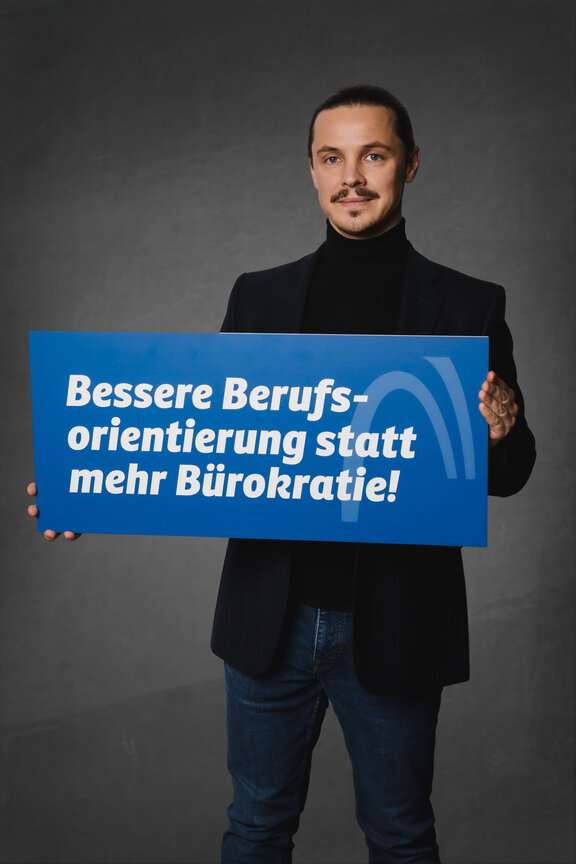 Eine Person steht vor einem neutralen grauen Hintergrund und hält ein großes blaues Schild mit der weißen Aufschrift: "Ja zur Ausbildung. Nein zur Abgabe!"