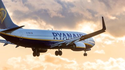 Zu sehen ist ein fliegendes Passagierflugzeig der Airline Ryanair im gelborangenen Abendhimmel.