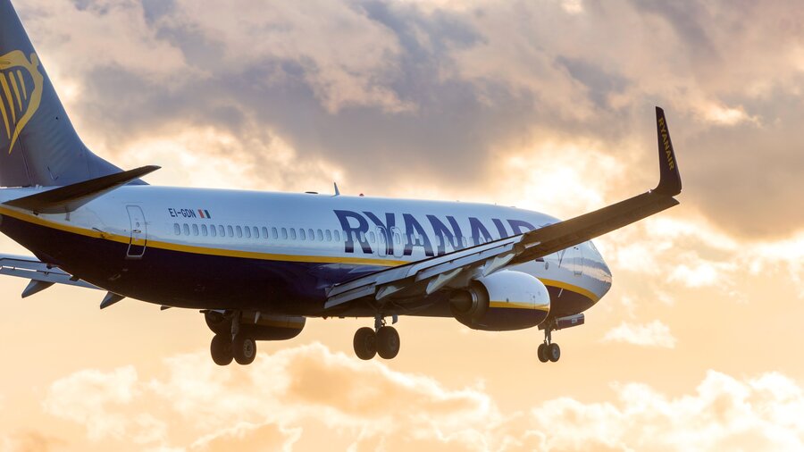 Zu sehen ist ein fliegendes Passagierflugzeig der Airline Ryanair im gelborangenen Abendhimmel.