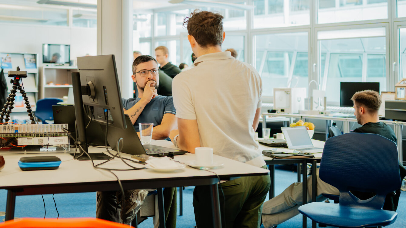 Berliner Unternehmerinnen und Unternehmenr beim Hackathon in Berlin sitzen an Tischen und denken nach.