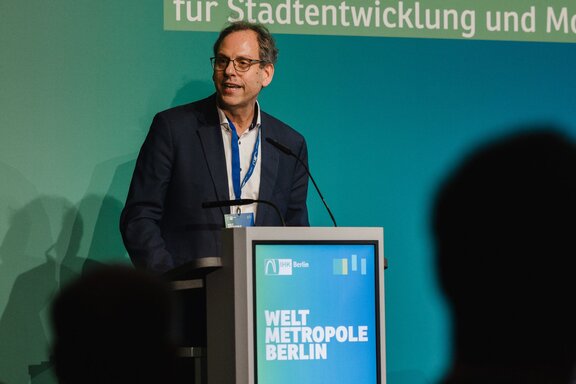 Ein Mann spricht auf einer Bühne vor Publikum.