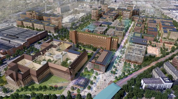Luftaufnahme eines modernen Stadtviertels mit mehreren mehrstöckigen Gebäuden, begrünten Flachdächern und einem zentralen Platz mit Bäumen und Menschen