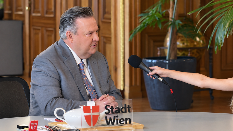 Zu sehen ist ein Mann im grauen Sakko, dem ein Mikrofon hingehalten wird. Es handelt sich um den Bürgermeister der Stadt Wien in einem Interview.