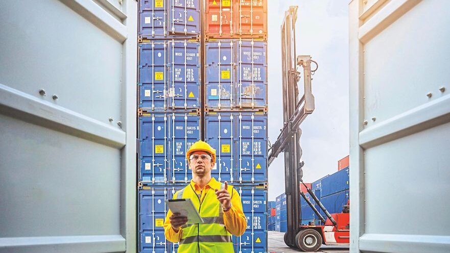 Foto eines Arbeiters in Warnweste mit Containern im Vorder- und Hintergrund