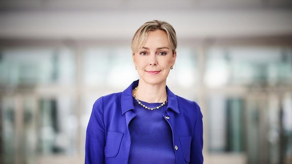 Auf dem Bild ist eine blonde Frau in einem blauen Kostüm zu sehen.