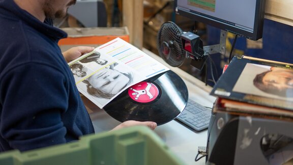 Zu sehen ist, wie die gebrauchten Artikel bei Momox sortiert und geprüft werden – hier anhand einer Schallplatte.