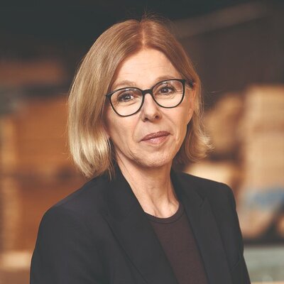 Zu sehen ist eine Frau mit Brille und etwa schulterlangen blonden Haaren, die neutral in die Kamera schaut. Sie trägt ein schwarzes Sakko.