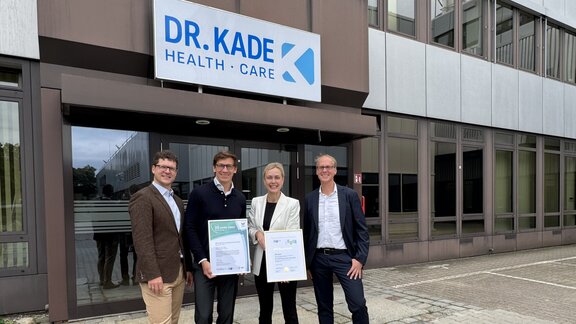 Drei Männer und eine Frau stehen vor einem Gewerbegebäude und halten zwei Urkunden in die Kamera, es sind die Geschäftsführer der Firma Dr. Kade und IHK-Hauptgeschäftsführerin Manja Schreiner