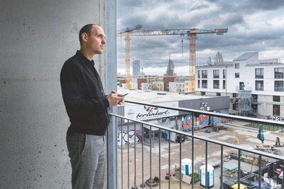 Mann mit visionärem Blick bedient sein Handy und blickt über eine Baustelle.