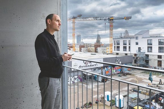 Mann mit visionärem Blick bedient sein Handy und blickt über eine Baustelle.