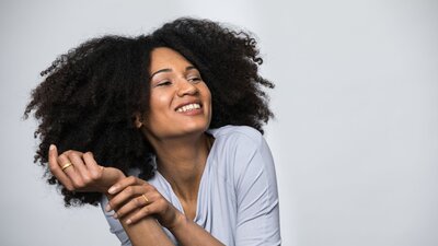 Zu sehen ist eine junge Frau mit lockigen braunen Haaren, die lächelnd zur Seite blickt.