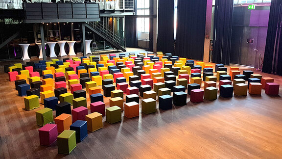 Viele bunte Sitzwürfel sind in Reihen in einem Theater aufgebaut. 