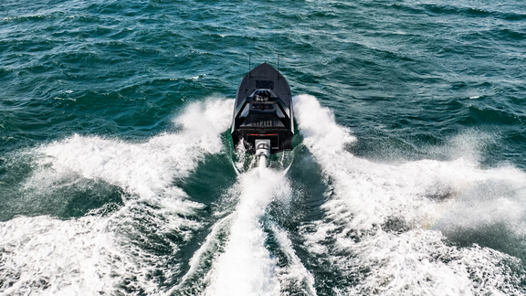 Schnelles schwarzes Motorboot fährt auf welliger Wasseroberfläche und erzeugt weiße Gischt.