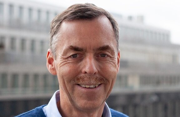 Das Bild zeigt Jürgen Grenz, einen weißen Mann mit blauem Hemd und Pullover, der freundlich in die Kamera guckt 