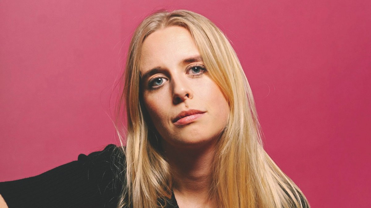 Eine Frau mit langen blonden Haaren und blauer Bluse sitzt lässig auf einem Stuhl