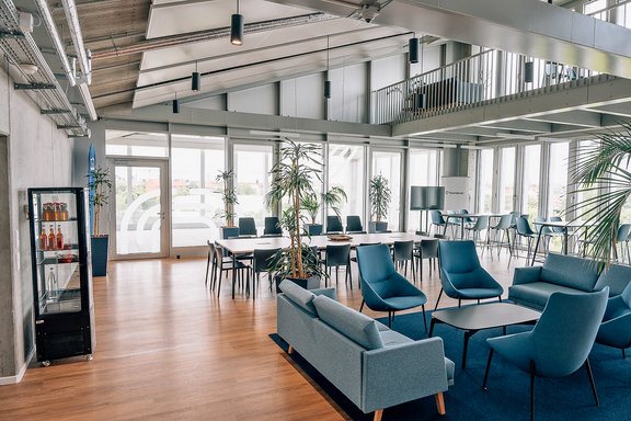 Helles, modernes Büro mit Sitzgruppen aus blauen Sesseln und Sofas, großen Fenstern und Pflanzen