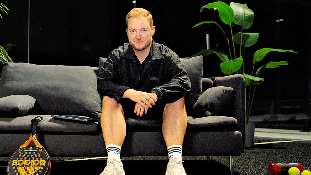 Ein Mann sitzt auf einem Sofa und lächelt in die Kamera. Es ist Bastian Krautwald von The Padel Company