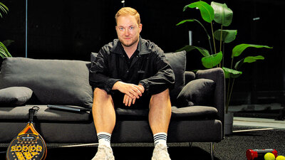 Ein Mann sitzt auf einem Sofa und lächelt in die Kamera. Es ist Bastian Krautwald von The Padel Company