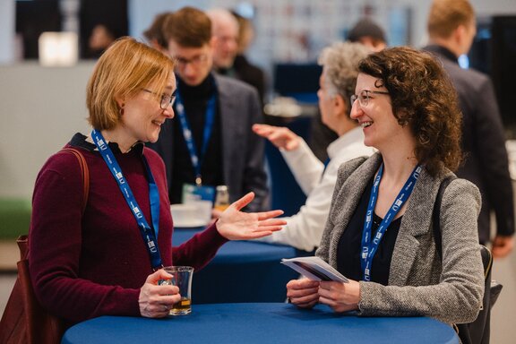 Zwei Frauen unterhalten sich an einem Stehtisch mit blauem Tischdeckchen.
