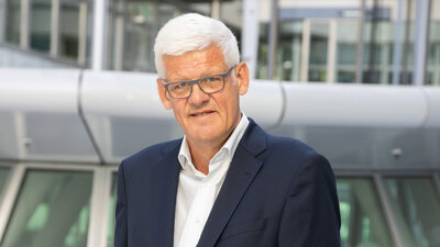 Thomas Groth steht im Anzug vor einem Gebäude 