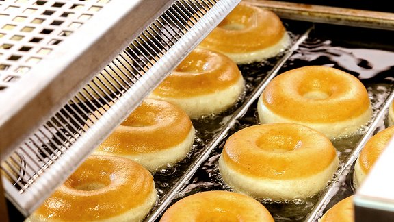 Frisch frittierte, goldbraune Donuts auf einem Förderband in einer Bäckerei