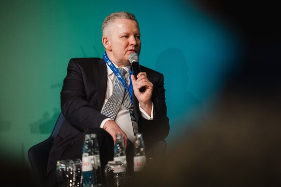 Ein Mann redet sitzend auf einer Bühne in ein Mokrofon.