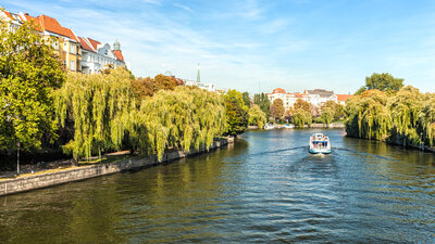 Zu sehen ist ein Fluss auf dem ein Schiff fährt. Es ist die Spree in Berlin.