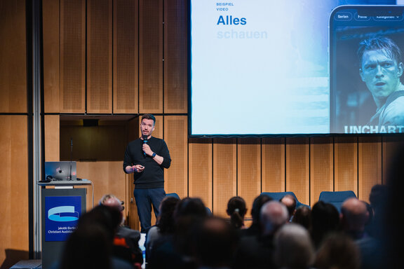 Vortragsszene beim Jakobb‑Kongress mit Präsentationsfolie im Hintergrund