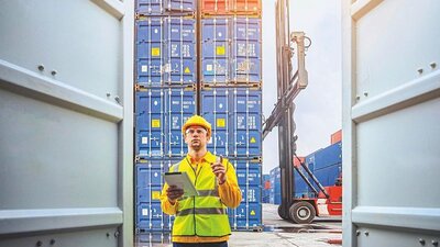 Foto eines Mannes in Warnweste mit mehreren Containern im Vorder- und Hintergrund