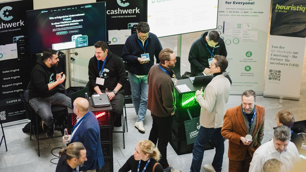 Zu sehen sind mehrere Menschen von oben, die sich auf einer Veranstaltung befinden und sich unterhalten. Es handelt sich um die DIGITAL+ Konferenz der IHK Berlin und HTW Berlin.