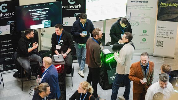 Zu sehen sind mehrere Menschen von oben, die sich auf einer Veranstaltung befinden und sich unterhalten. Es handelt sich um die DIGITAL+ Konferenz der IHK Berlin und HTW Berlin.