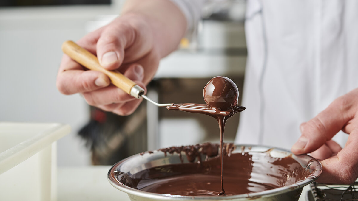 Ein Mann glasiert eine Praline mit Schokolade
