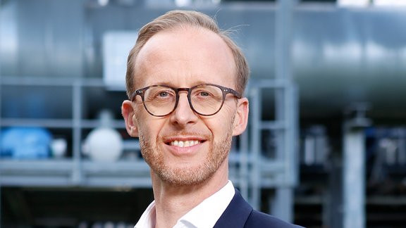 Lächelnder Mann mit Brille in dunkelblauem Anzug und weißem Hemd vor modernem Gebäude