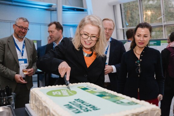 Zu sehen ist eine blonde Frau, die eine rechteckige Torte anschneidet. Es handelt sich um die Berliner Senatorin Ute Bonde.