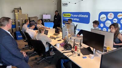 Auf dem Bild sind einige Menschen zu sehen, die gemeinsam um mehrere Schreibtische herum sitzen und am Computer arbeiten. 