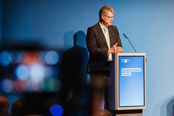 Zu sehen ist ein älterer Herr im Anzug an einem Redepult. Es handelt sich um Bundesverkehrsminister Patrick Schnieder.