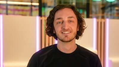 Ein junger Mann im schwarzen Sweater steht vor einer beleuchteten Wand. Es ist der COO von 1Komma5°, Alexander Brenske