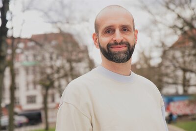 Auf dem Bild ist ein Mann mit Bart und Glatze zu sehen, der in die Kamera lächelt.