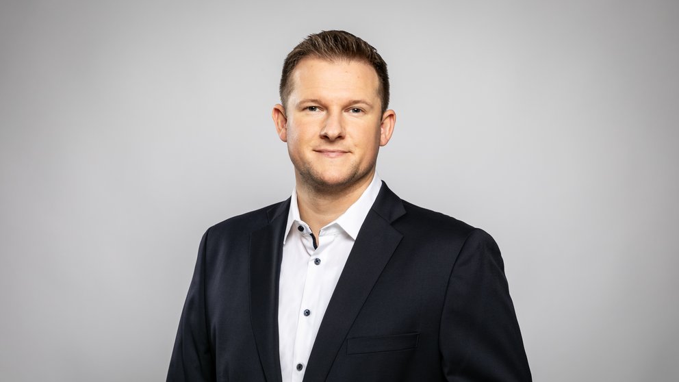 Michael Blaumoser, CEO von Sius Consulting in schwarzem Anzug vor einem grauen Hintergrund