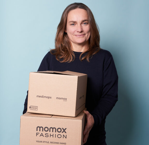Claudia Frese, Geschäftsführerin von Momox, hält Kartons mit der Aufschrift „momox Fashion“ in den Händen.