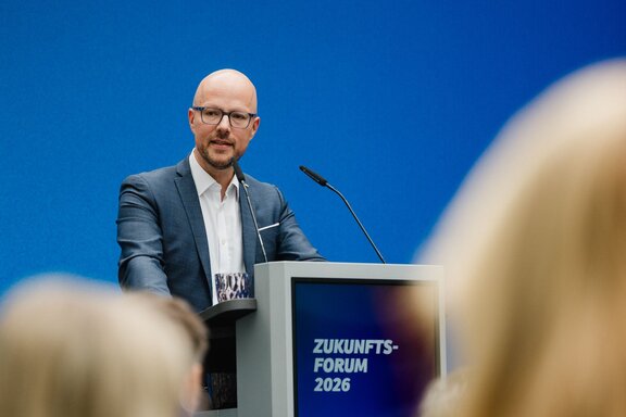 Zu sehen ist ein Mann mit Glatze und Brille hinter einem Redepult. Es handelt sich um Sebastian Stietzel.
