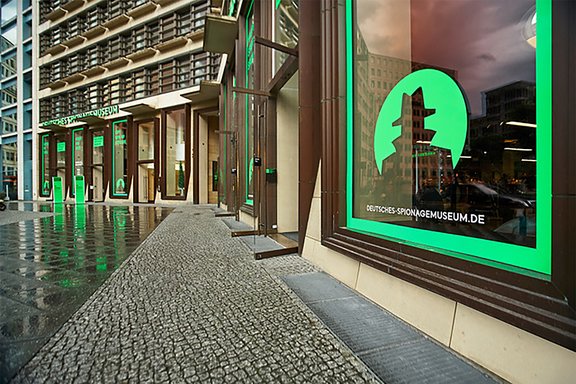 Fassade des Deutschen Spionagemuseums mit grünem Logo und Schriftzug 'deutsches-spionagemuseum.de' an Fenstern eines modernen Gebäudes